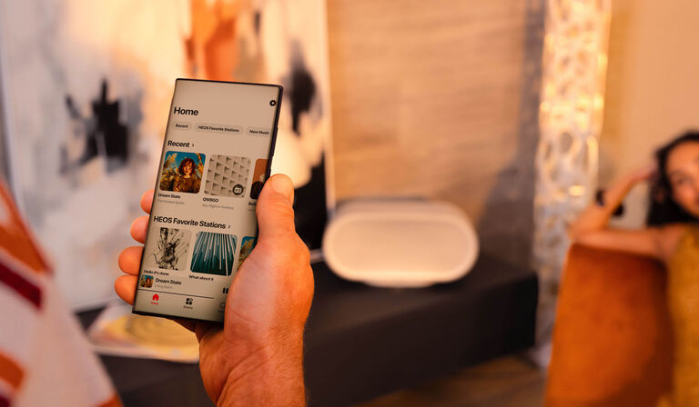 A person using the HEOS app to control a Denon Home Speaker