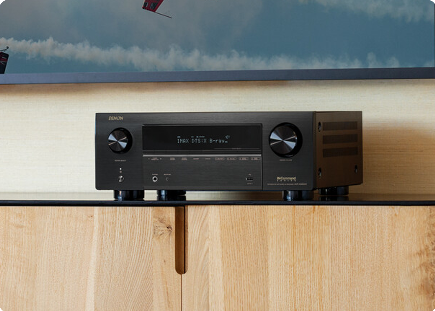 AVR-X3800H on a tv stand under a tv displaying airplanes