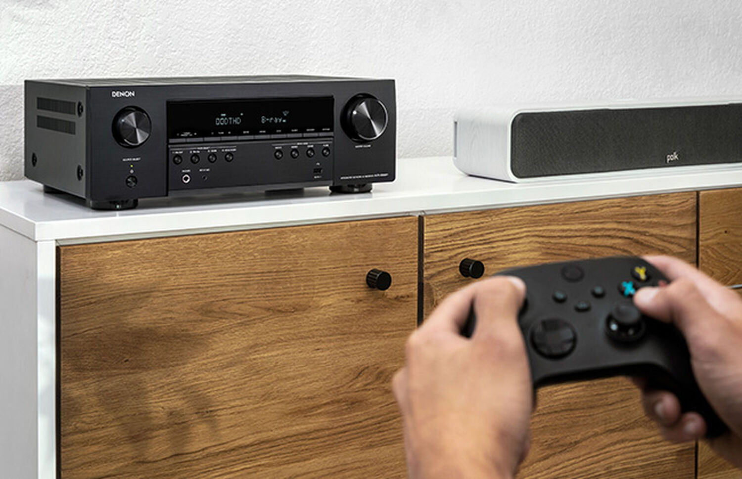 a man holding a gaming console controller with an AVR in the background