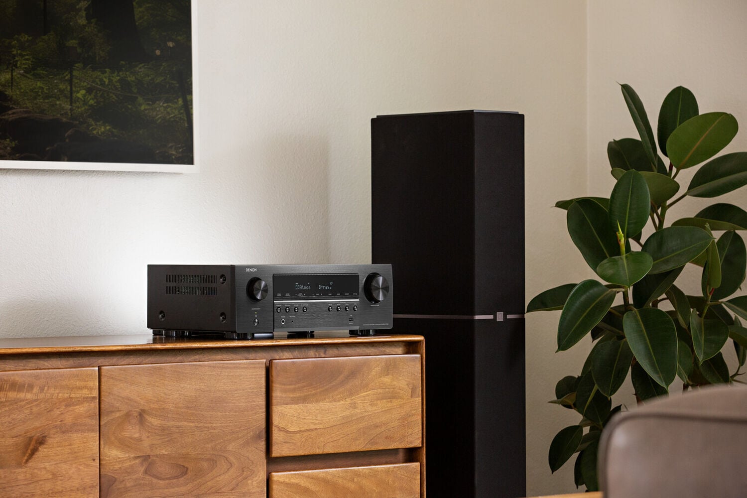 An S-Series AVR on a tv stand next to a floor standing speaker