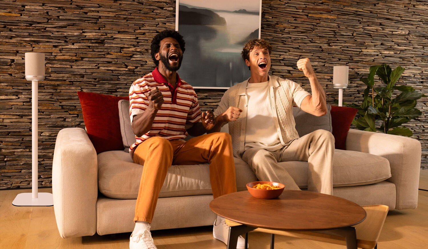 Men on a couch cheering, with Denon Home 200s as rears subtly off to the side